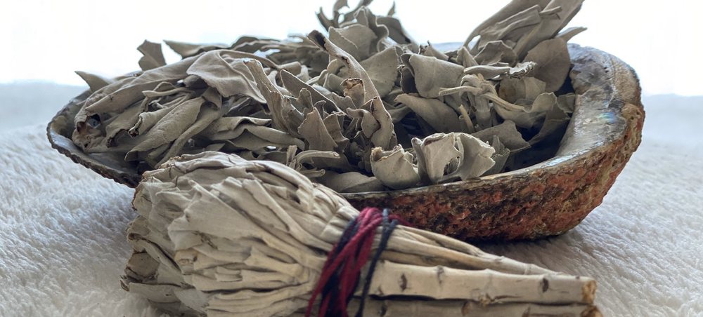 A bundle of dried sage beside an abalone shell holding loose sage leaves