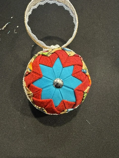 A finished ornament in red and turquoise, folded into an eight-pointed star with a button at the centre, beside a loop of lace ready to be attached.