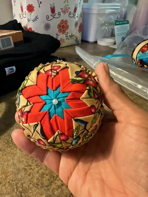 A hand holding a cream and red ornament, the fabric points fanning out from a centre stud, in the craft room.