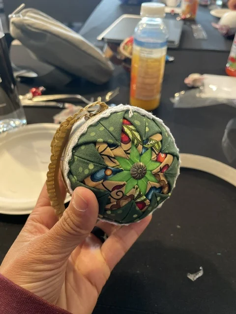 The same green ornament held up closer to the camera, the folded points and centre button clearly visible.