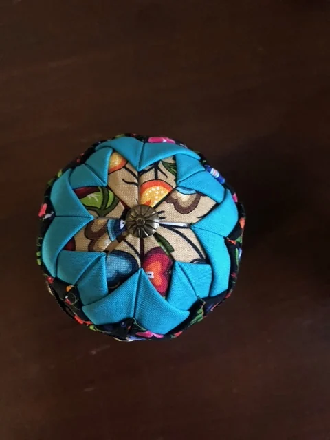 A turquoise and cream ornament on a dark surface, the fabric points overlapping around a small centre button.