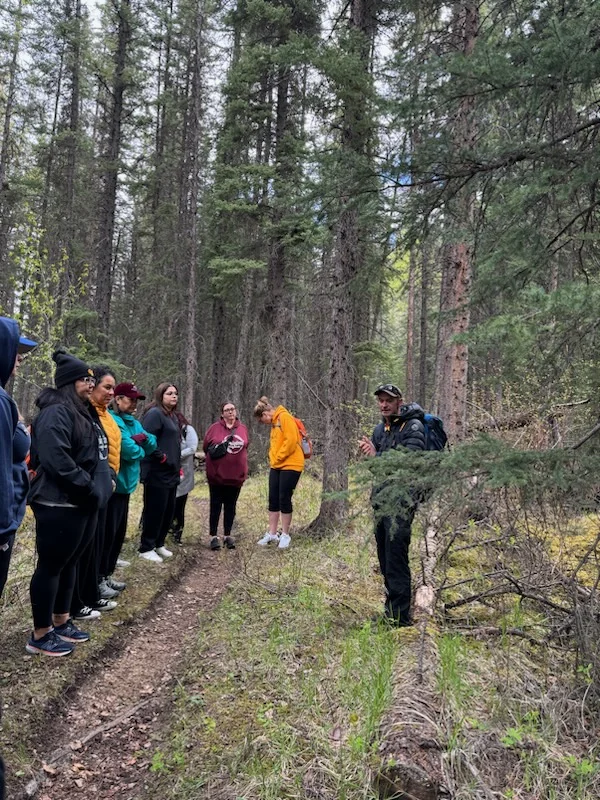 The group gathered in a clearing in the trees, listening to someone speaking at the edge of the trail.