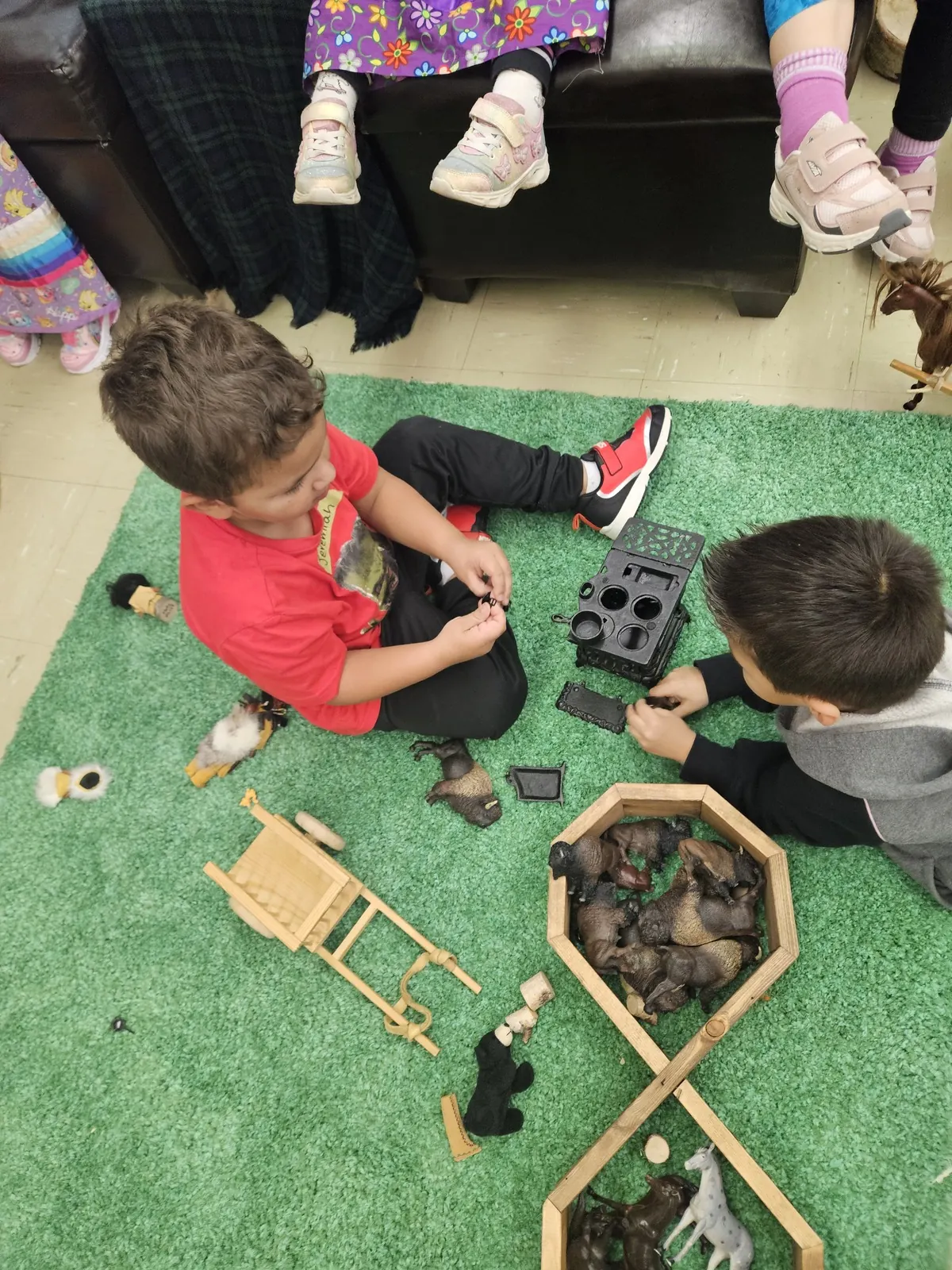 Two children playing with carved animals and a small wooden frame on a green play mat.