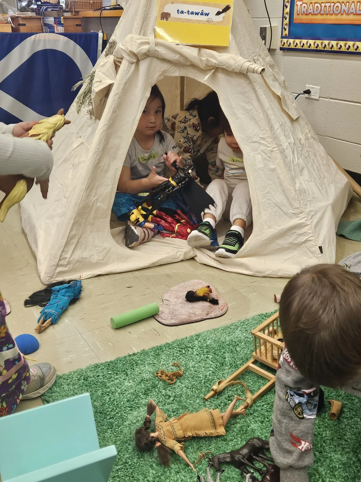 Children playing around the tipi with wooden animals and a small drying rack.