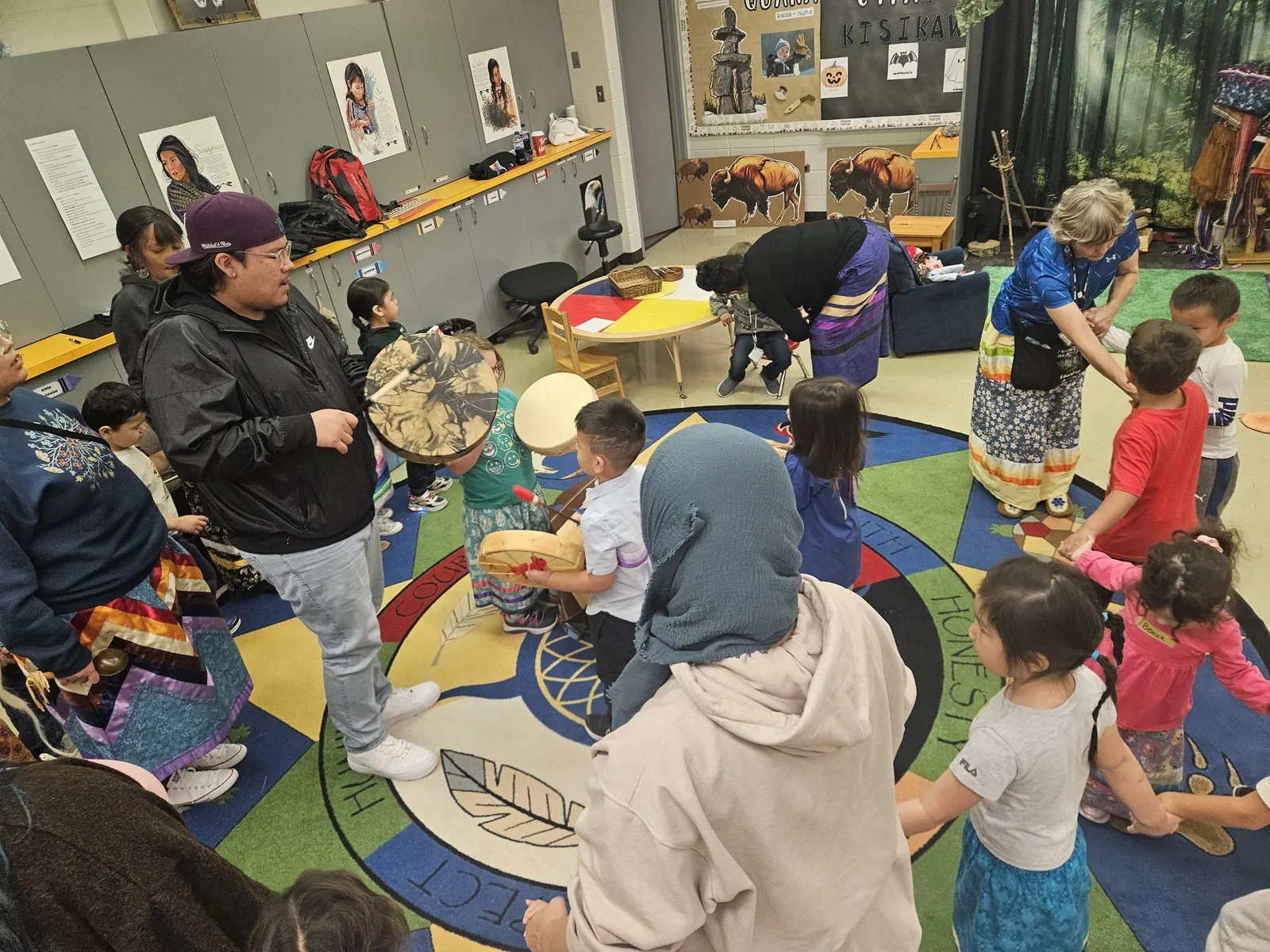 Staff standing with hand drums as the children gather around them.