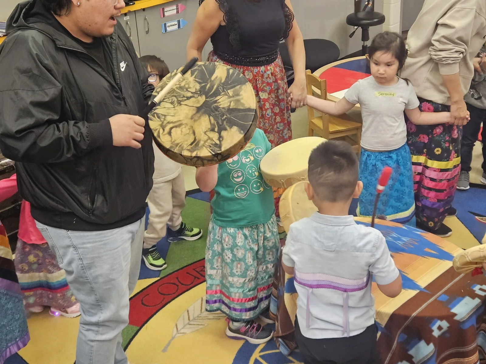 A drummer leading while children hold their own drums and watch.