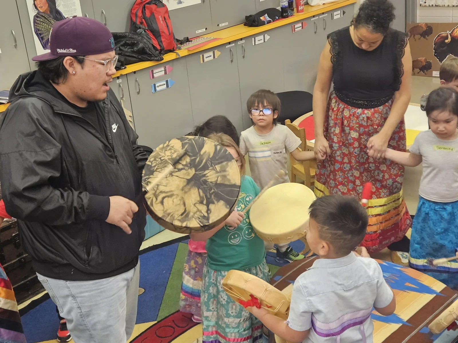 Children standing in a line with their drums, a staff member drumming in front.