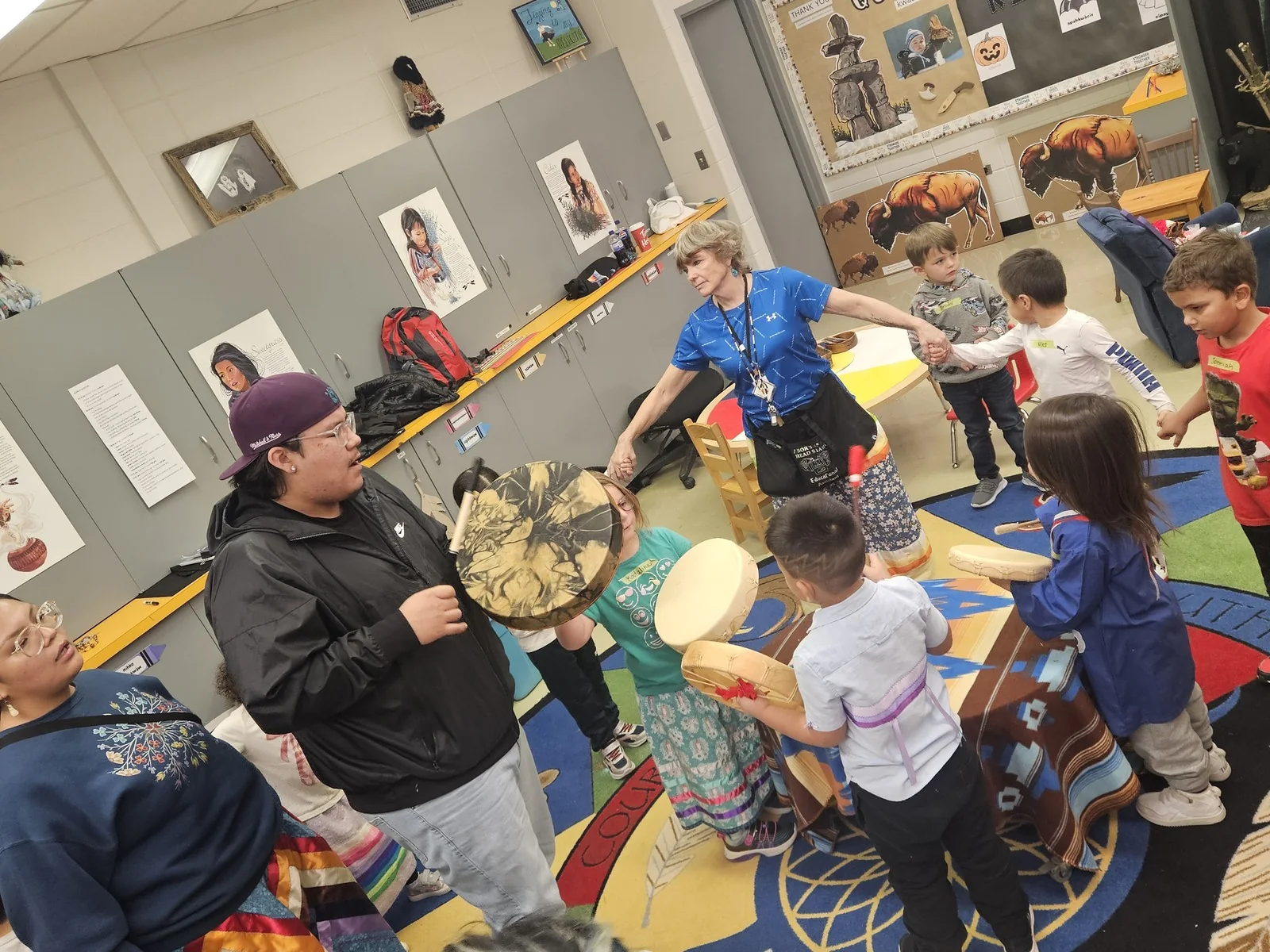 Children and staff drumming together in the middle of the room.