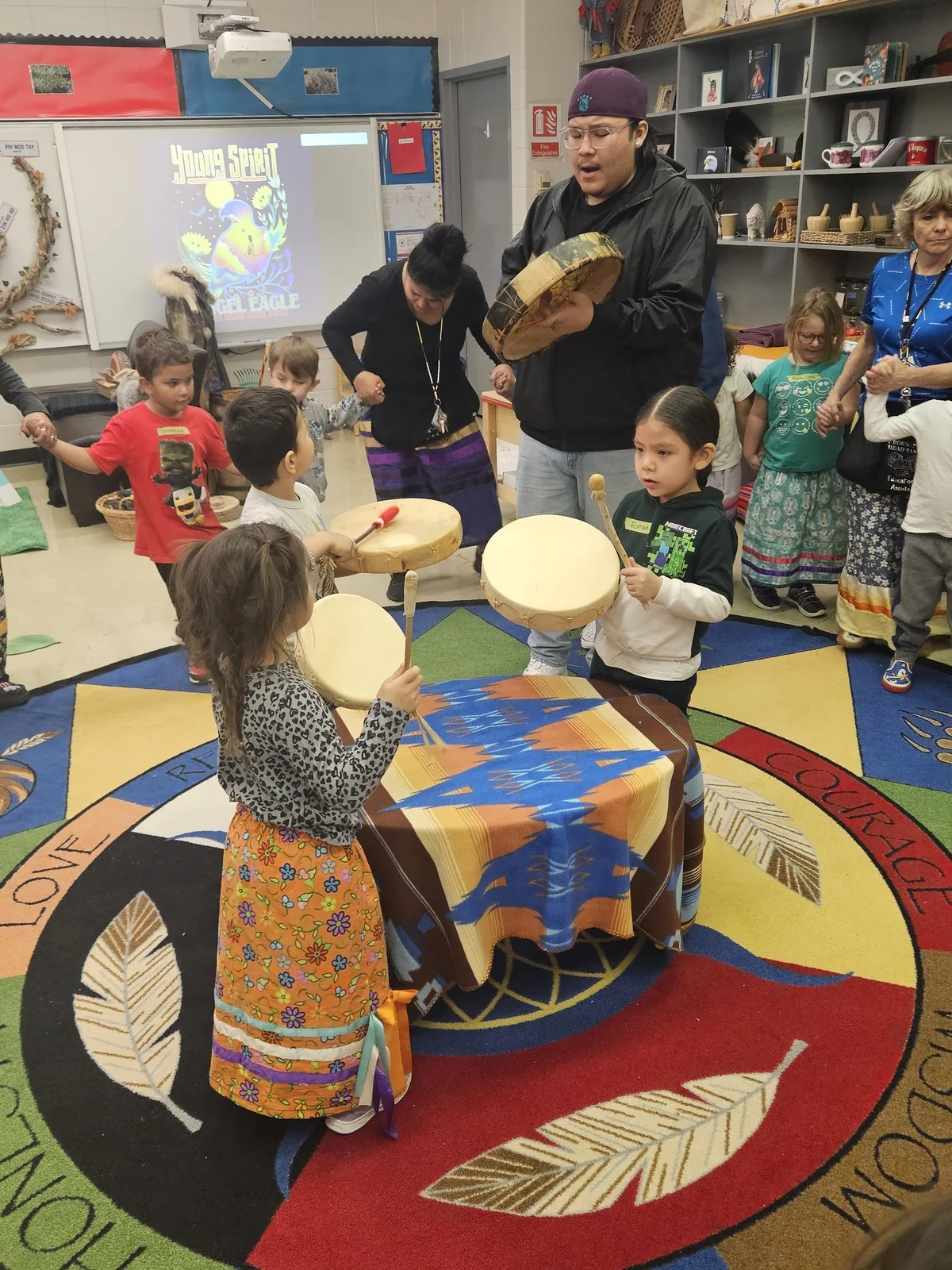 The dance continuing, children and staff drumming around the edge.