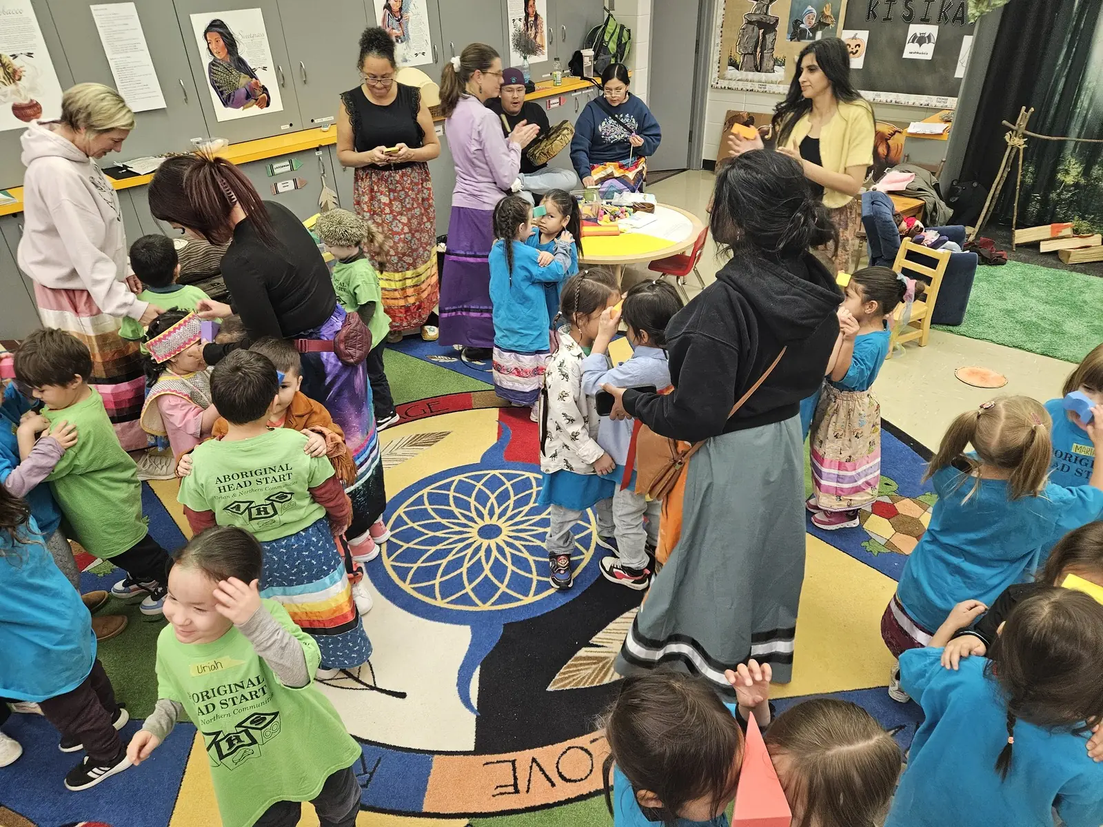 Staff in ribbon skirts standing among the children during the round dance.