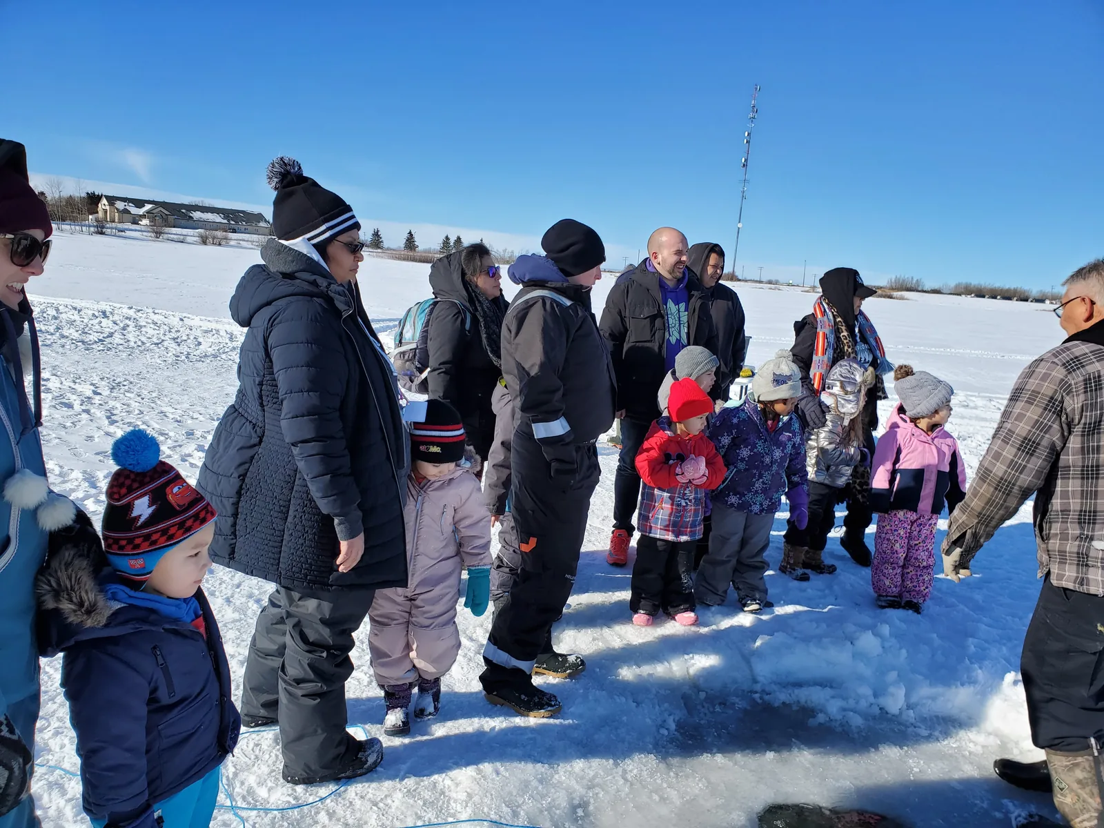 The group out on the frozen lake under a clear blue sky, children and adults bundled against the cold.