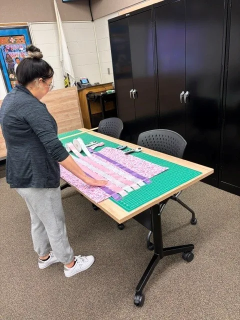 A woman arranging strips of ribbon and fabric in rows on a green cutting mat, working out the order of the bands.
