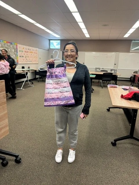 A woman holding up a finished purple and lilac ribbon skirt on a hanger.